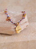 Bracelet with colorful beads and a gold charm on a stone surface