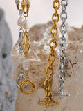 Three gold and silver chain necklaces on a textured stone surface.